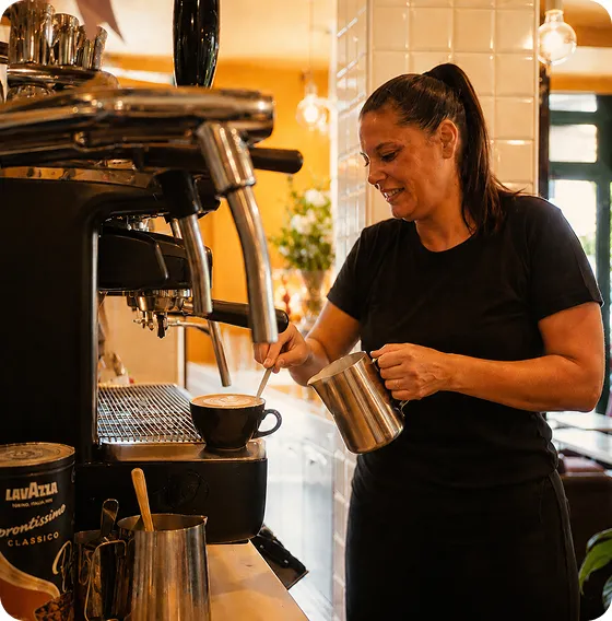 dipendente del caffe dell'orologia a maranello che prepara un cappuccino italiano per dei turisti che hanno in programma di visitare il museo ferrari